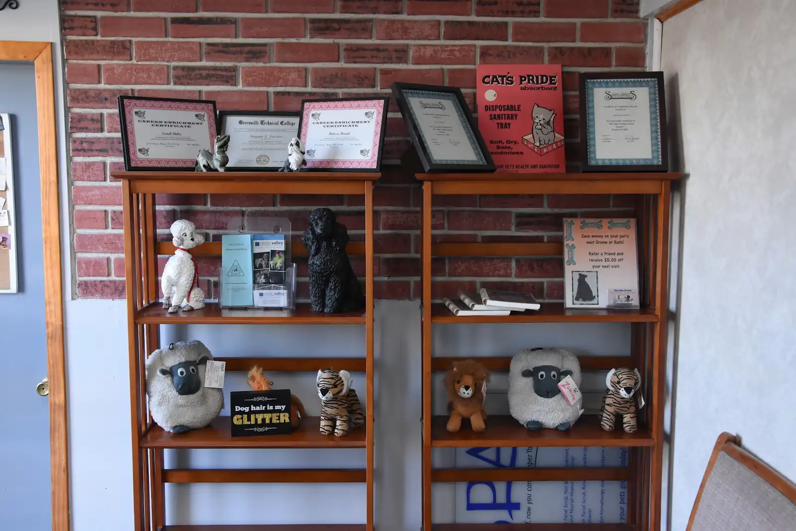 The reception shelves at Shear Bliss: framed certificates on a brick wall above poodle figurines and plush toys